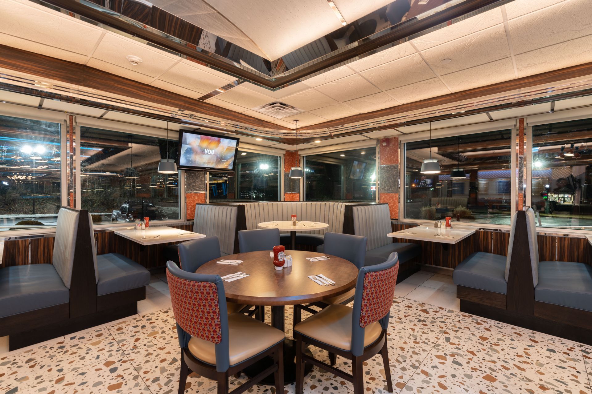 A restaurant with tables and chairs and a television on the ceiling.