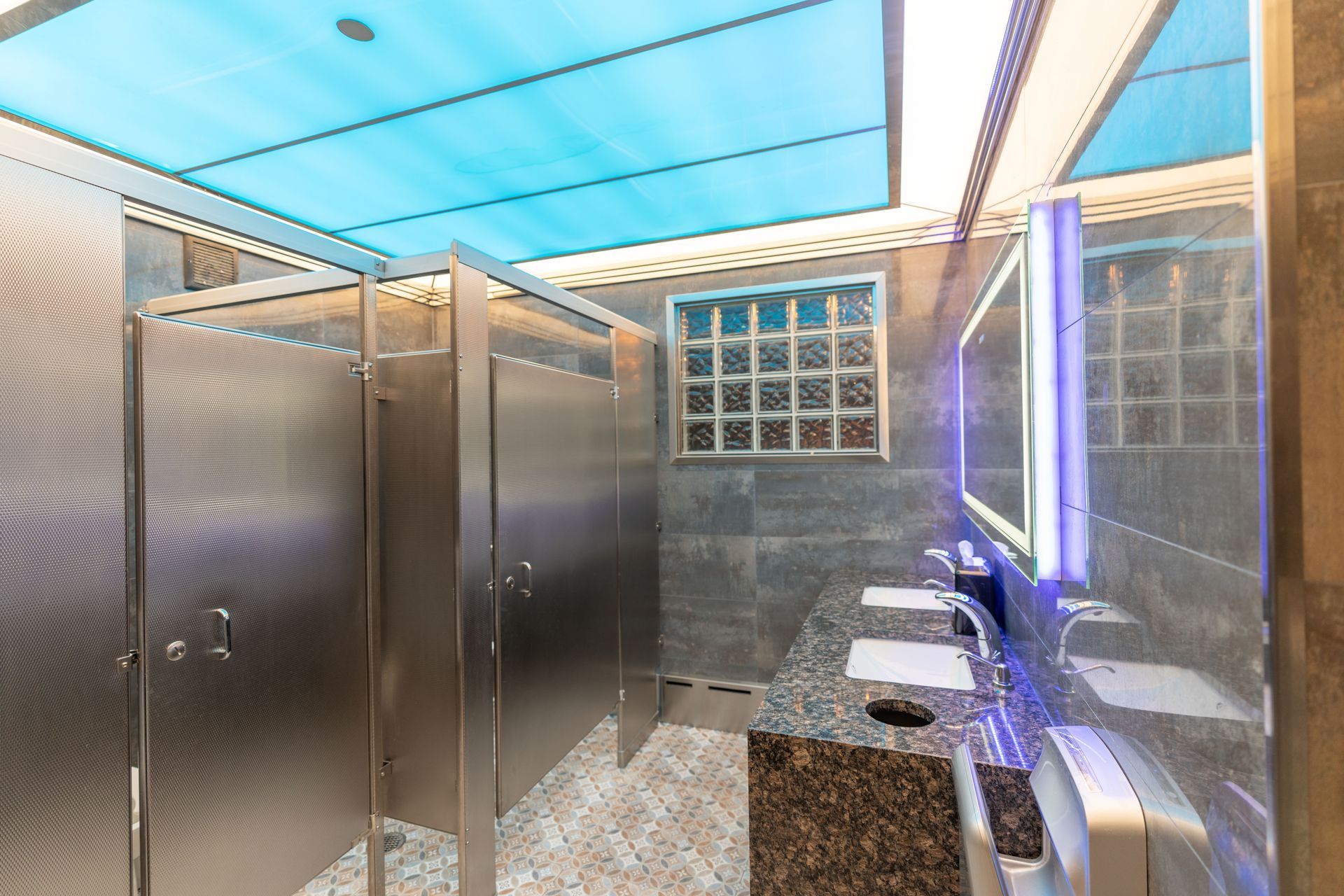 A public restroom with stainless steel stalls and a sink.