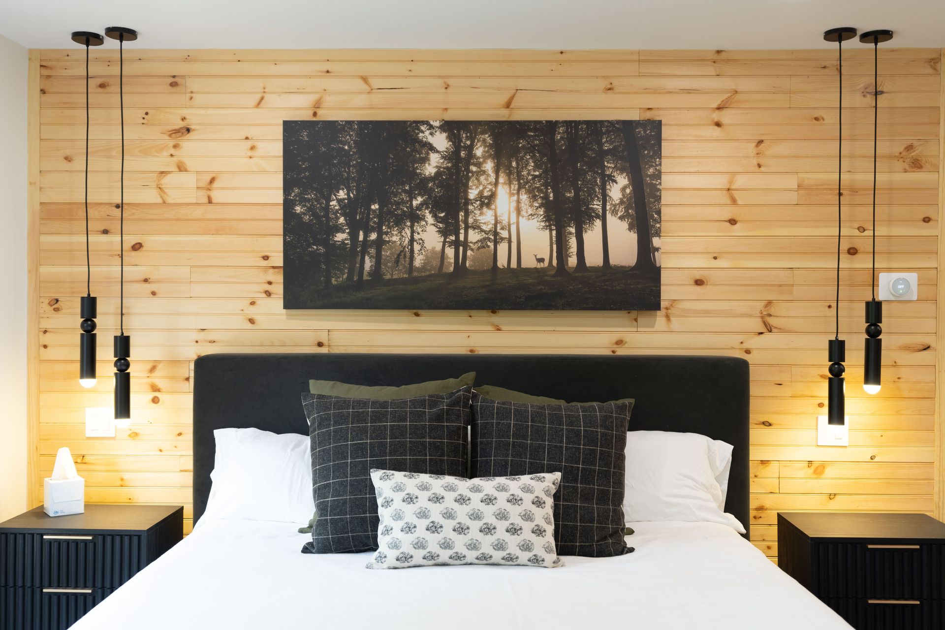 A bedroom with a painting of trees on the wall above the bed