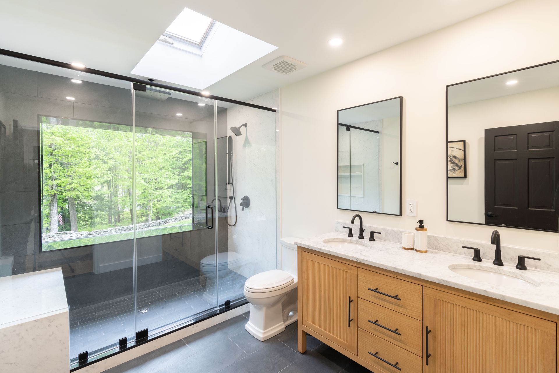 A bathroom with two sinks , a toilet , and a skylight.