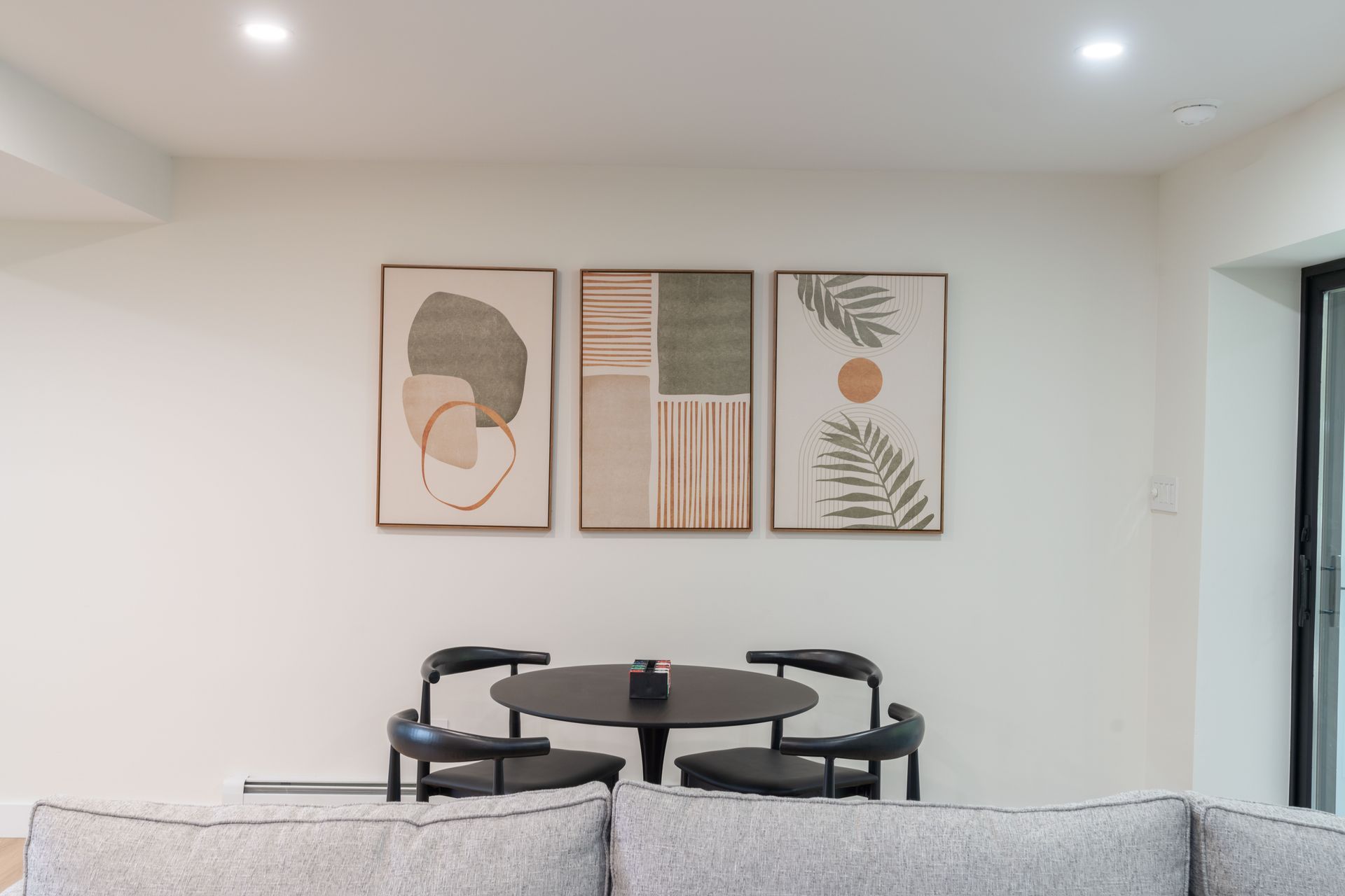 A living room with a couch , table and chairs and three paintings on the wall.