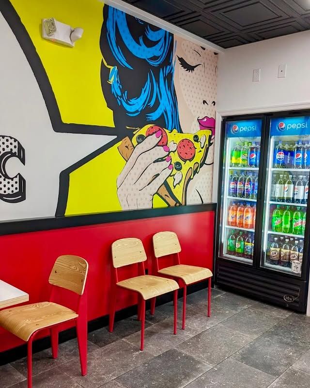 A restaurant with a mural of a woman eating a pizza on the wall