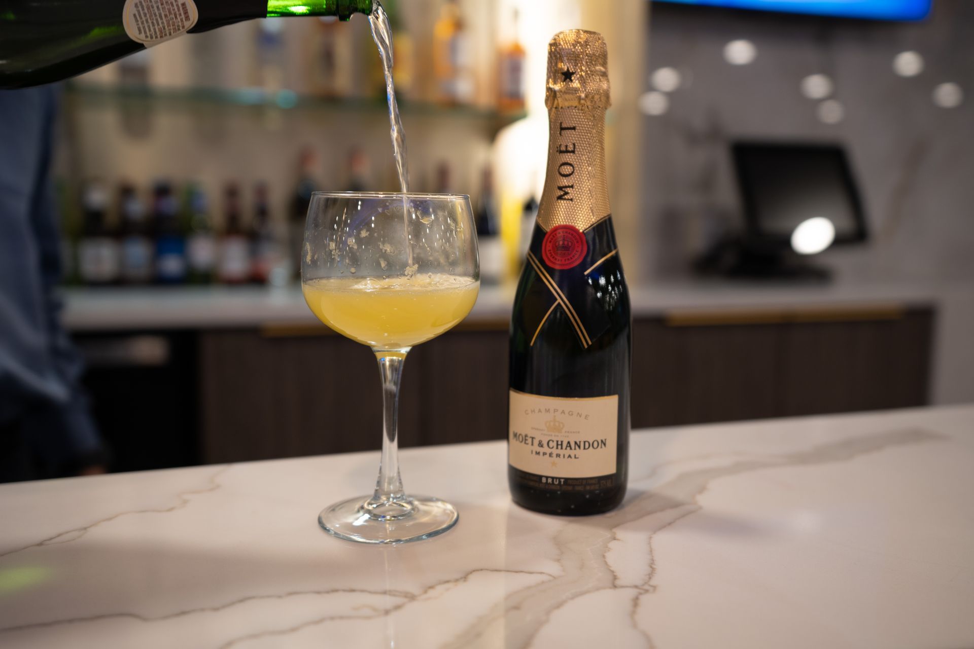 A bottle of champagne is being poured into a glass on a bar.