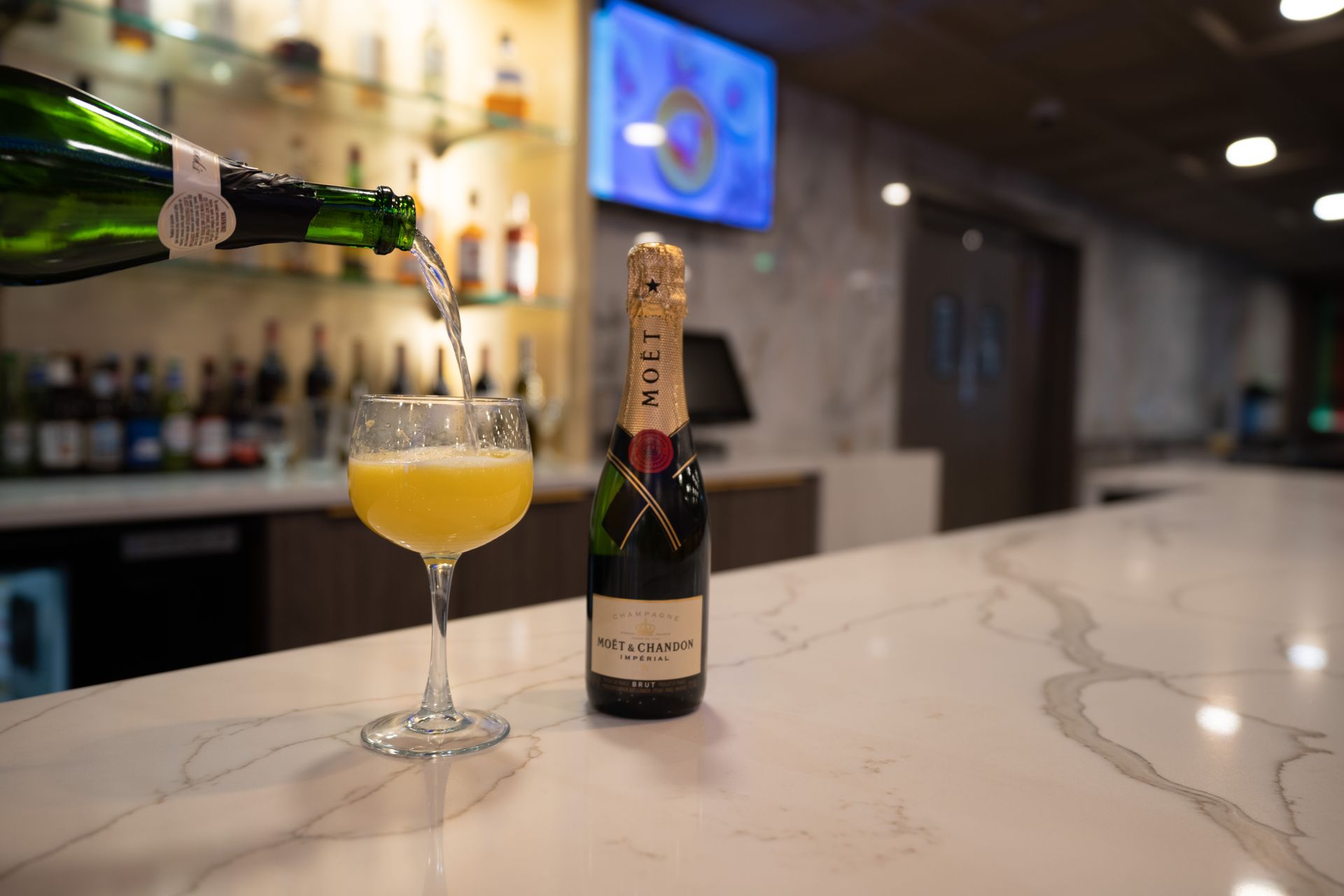 A bottle of champagne is being poured into a glass on a bar.
