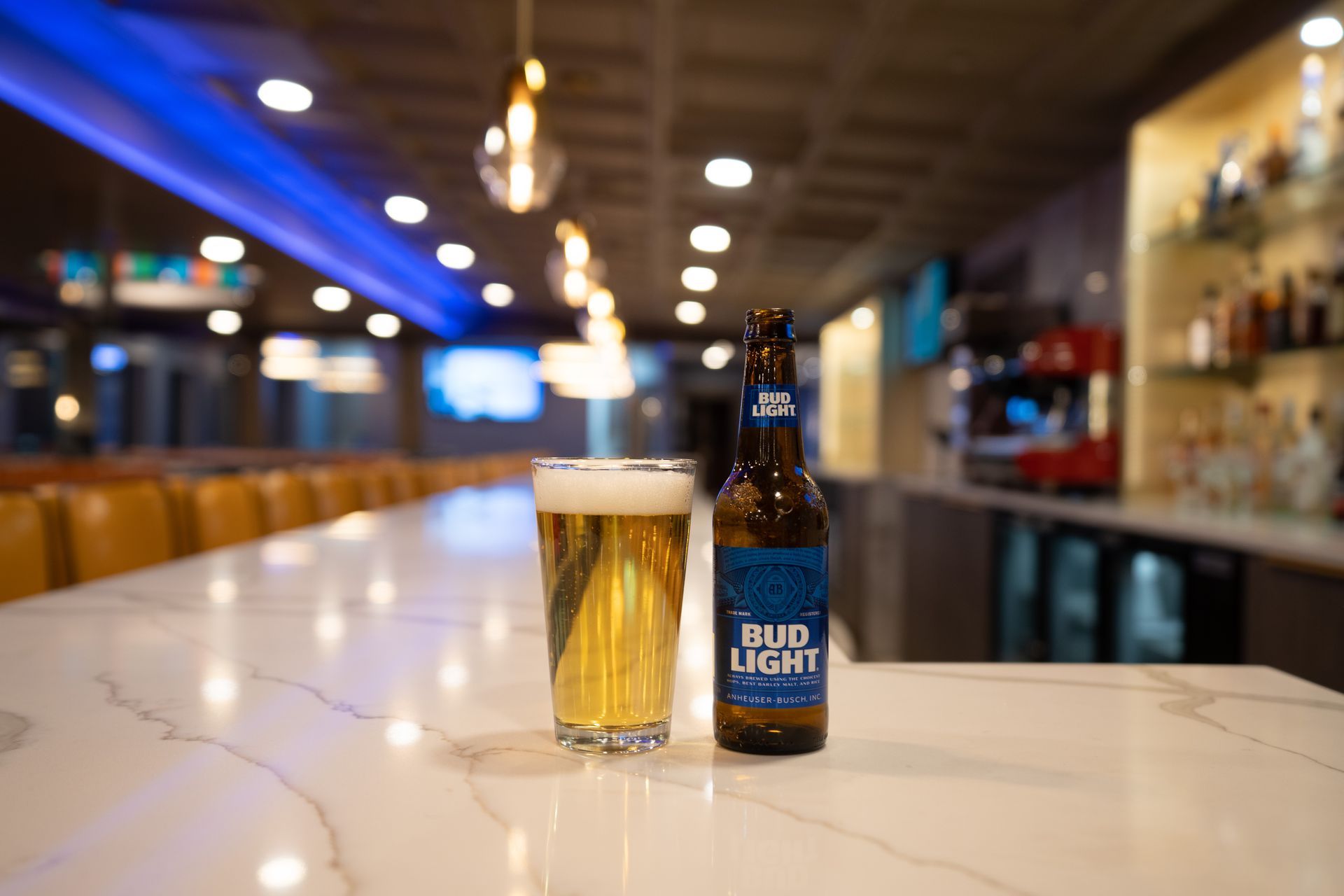 A bottle of bud light beer and a glass of beer are on a bar counter.