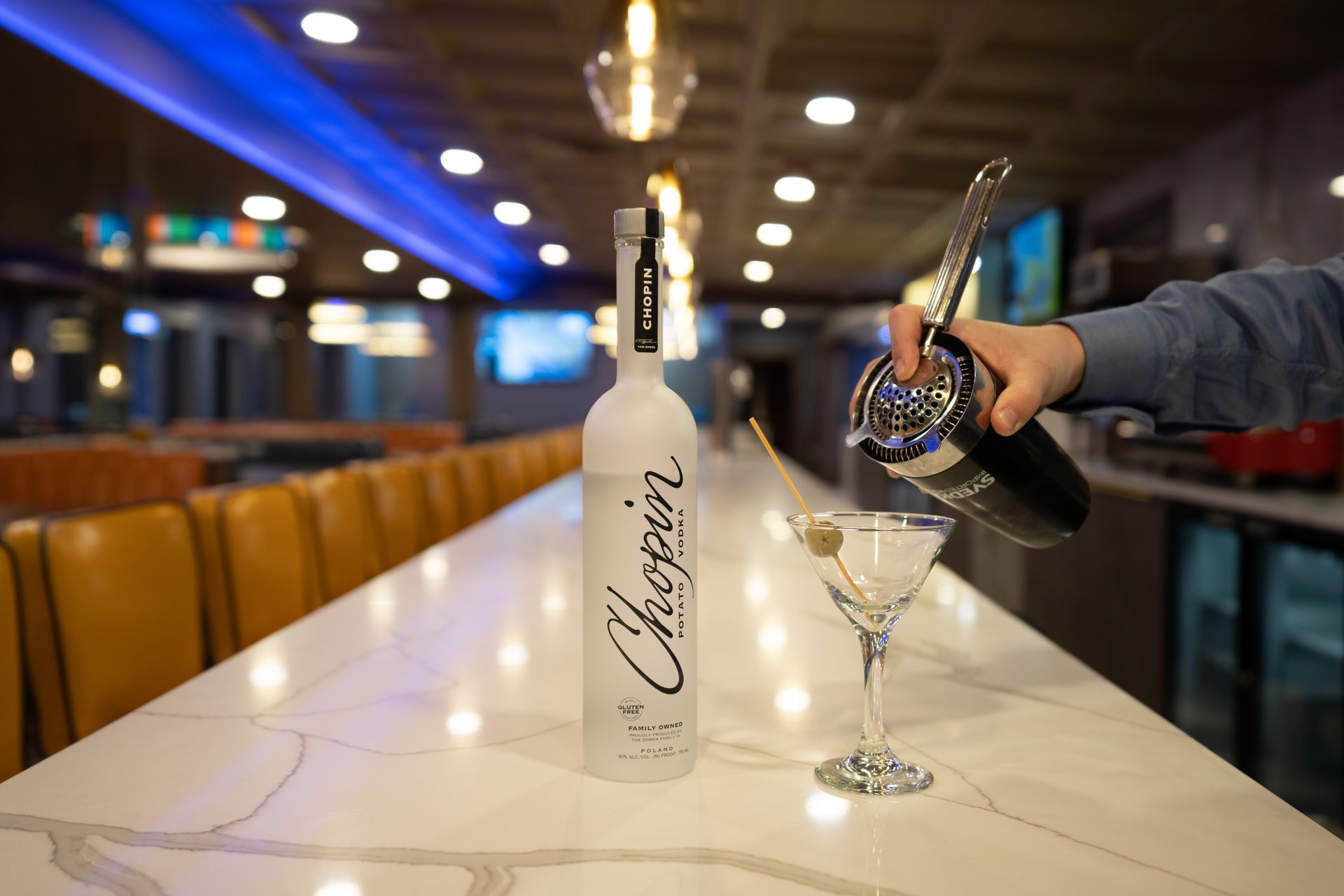 A person is pouring a martini into a glass next to a bottle of chopin vodka.