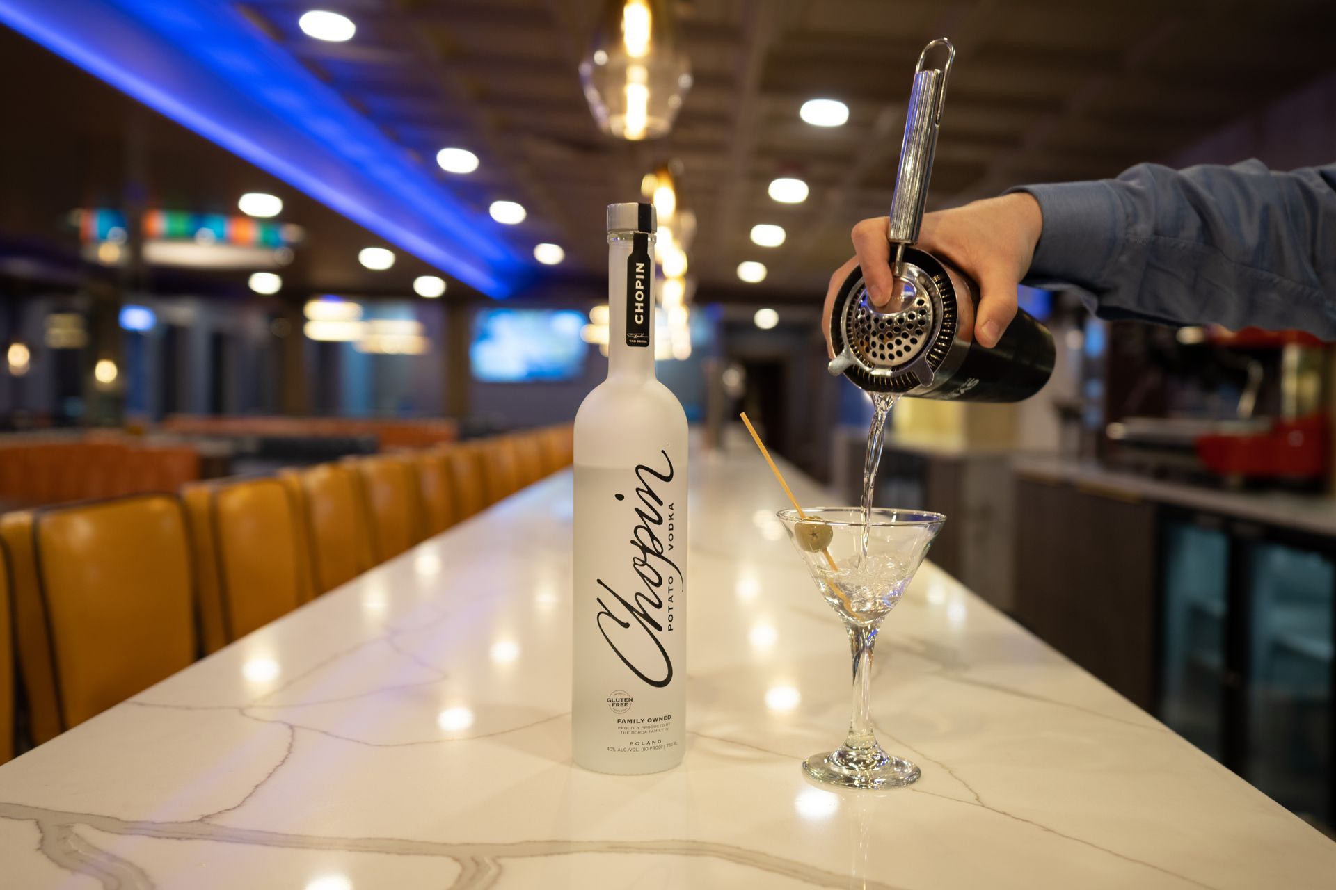 A person is pouring a martini from a shaker into a glass.