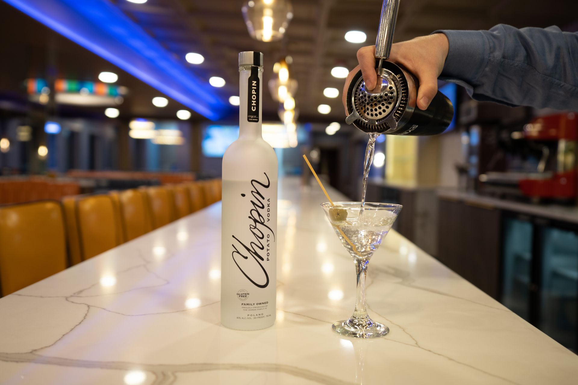 A person is pouring a martini into a martini glass.