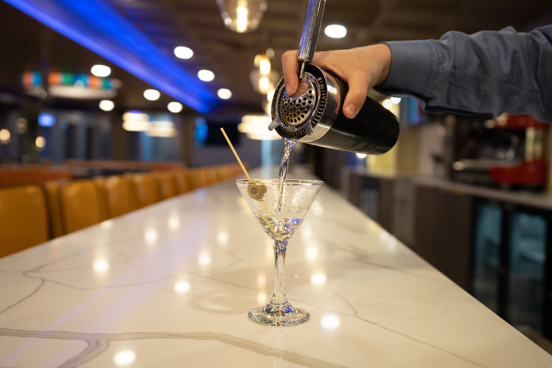 A bartender is pouring a martini into a martini glass.