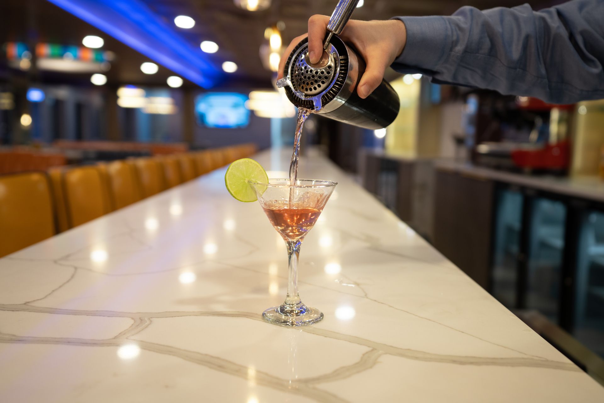 A bartender is pouring a drink into a martini glass.