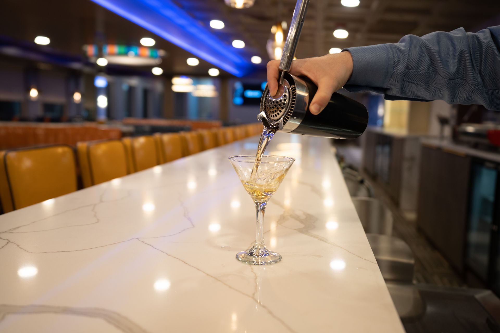 A person is pouring a martini into a glass on a bar.