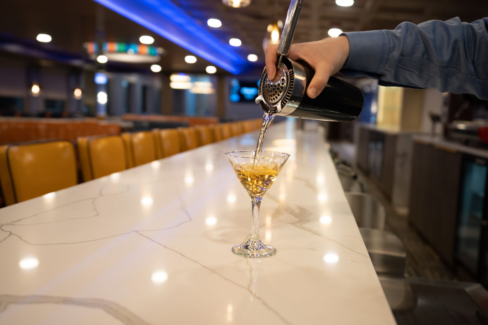 A person is pouring a martini into a glass on a bar.