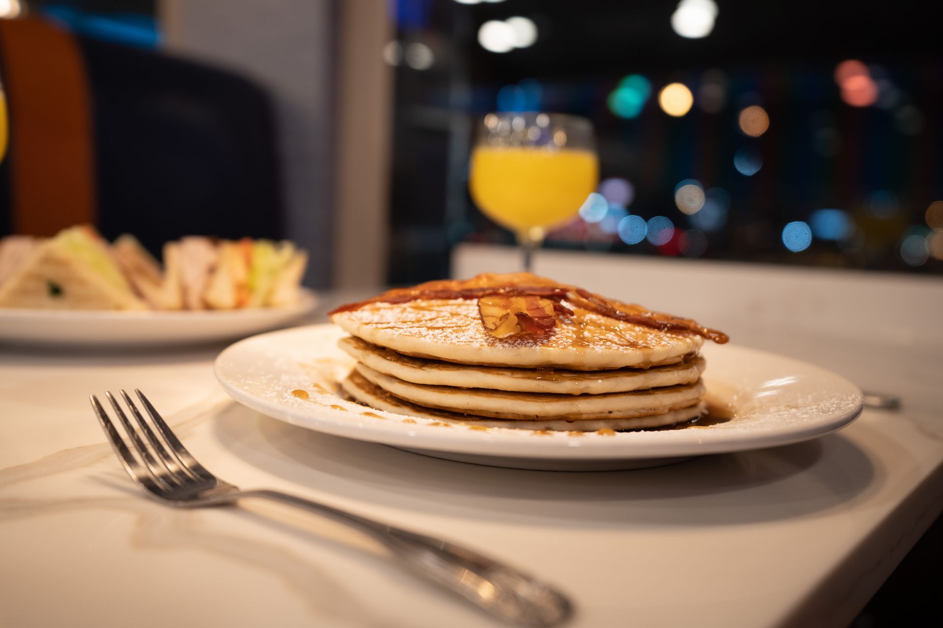 A stack of pancakes on a plate with a fork and a glass of orange juice.