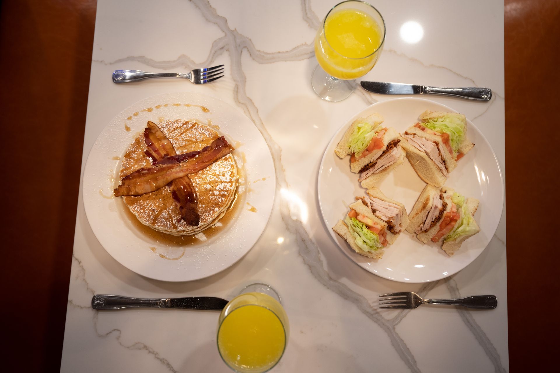 A table topped with plates of food including pancakes and sandwiches.