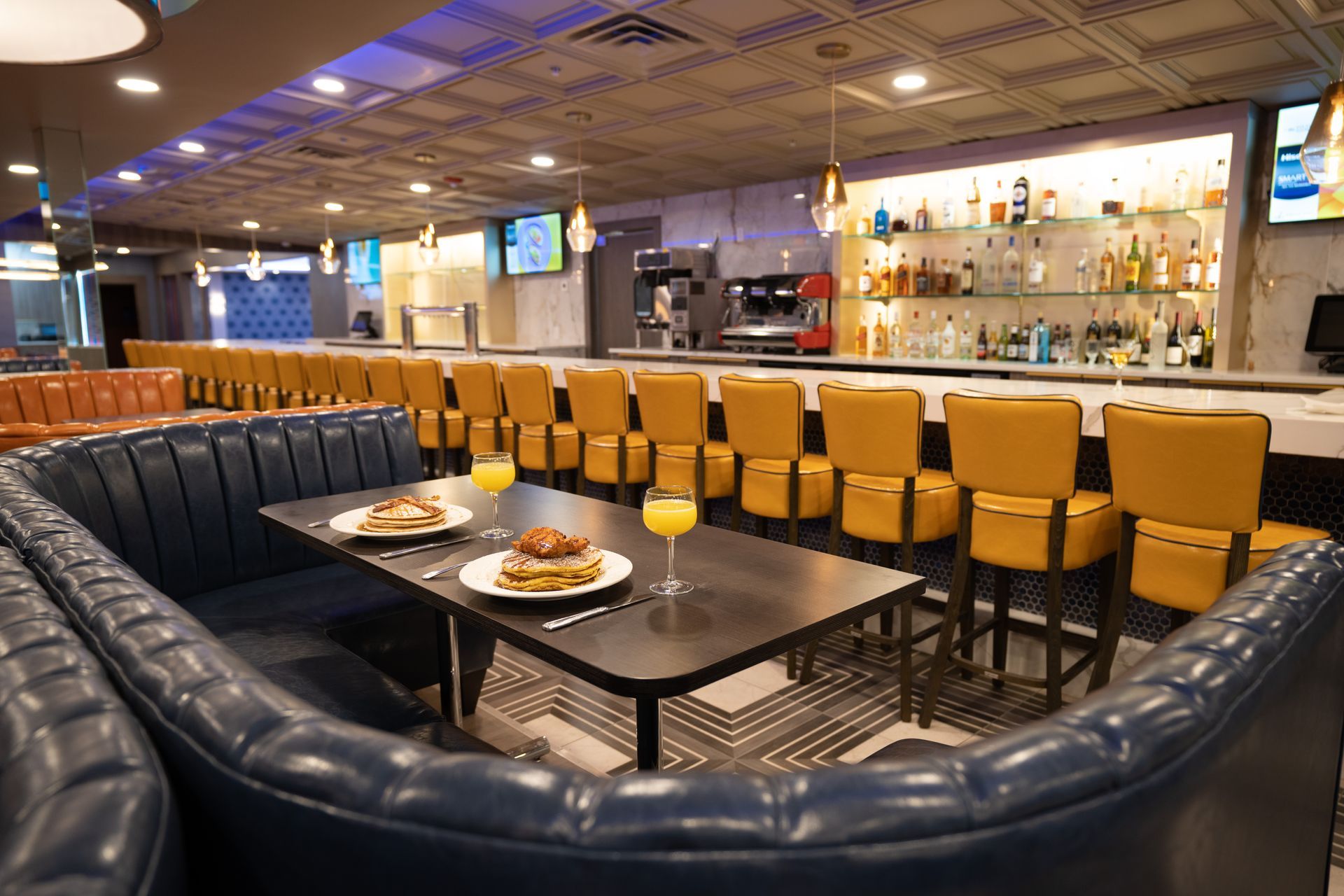 A restaurant with a long bar and tables with plates of food on them.
