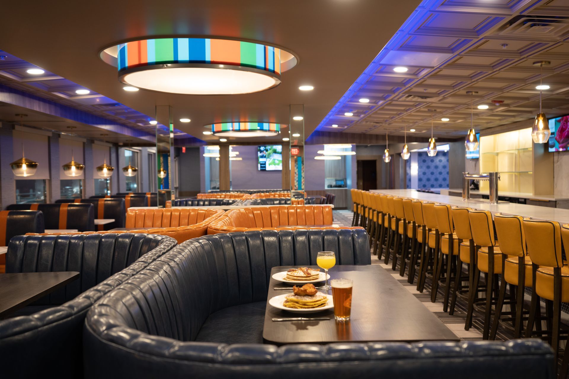 A restaurant with tables and chairs and a long bar.