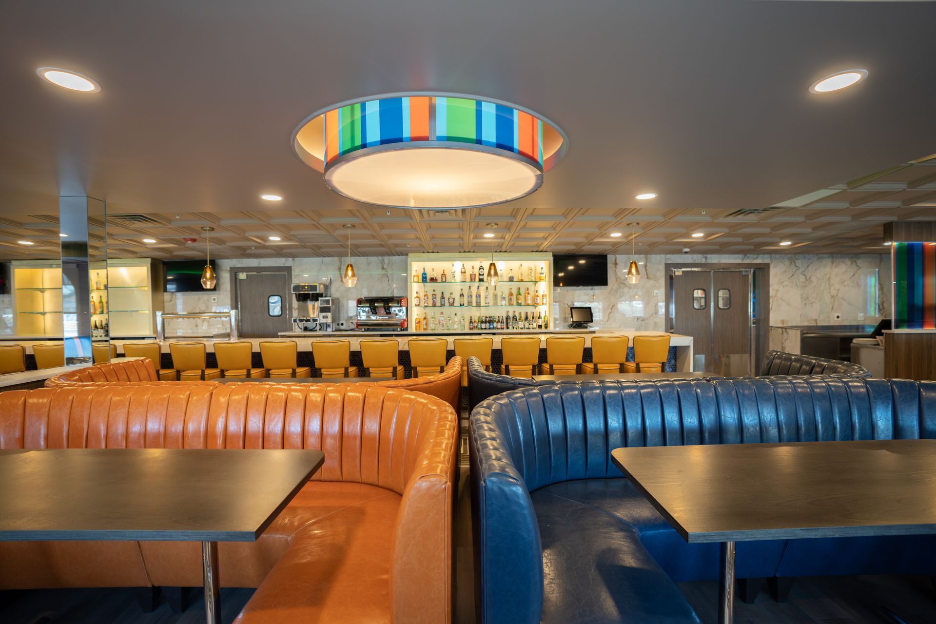 A restaurant with tables and couches and a bar in the background.