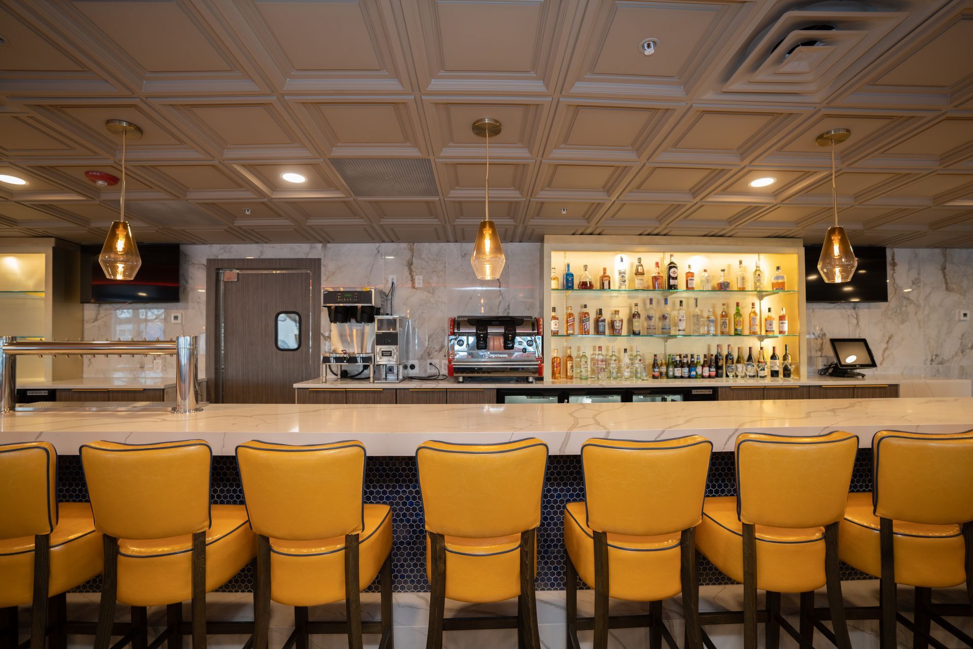 A restaurant with a long bar and yellow chairs.