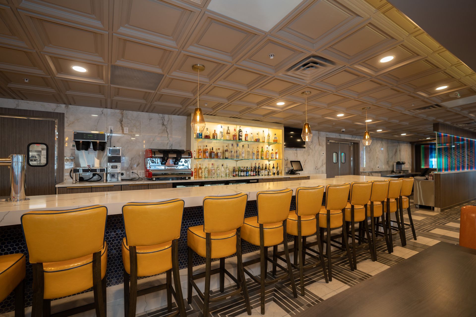 A restaurant with a long bar and yellow chairs.