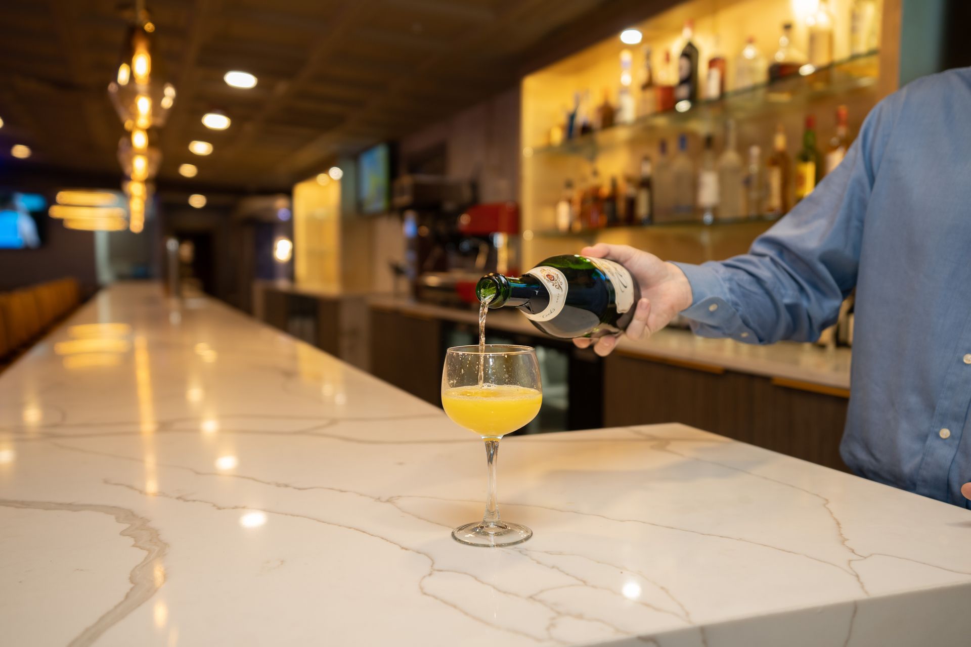 A man is pouring a drink into a glass at a bar.