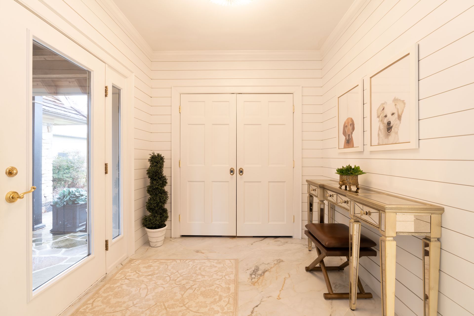 A hallway with white walls , a table and a bench.