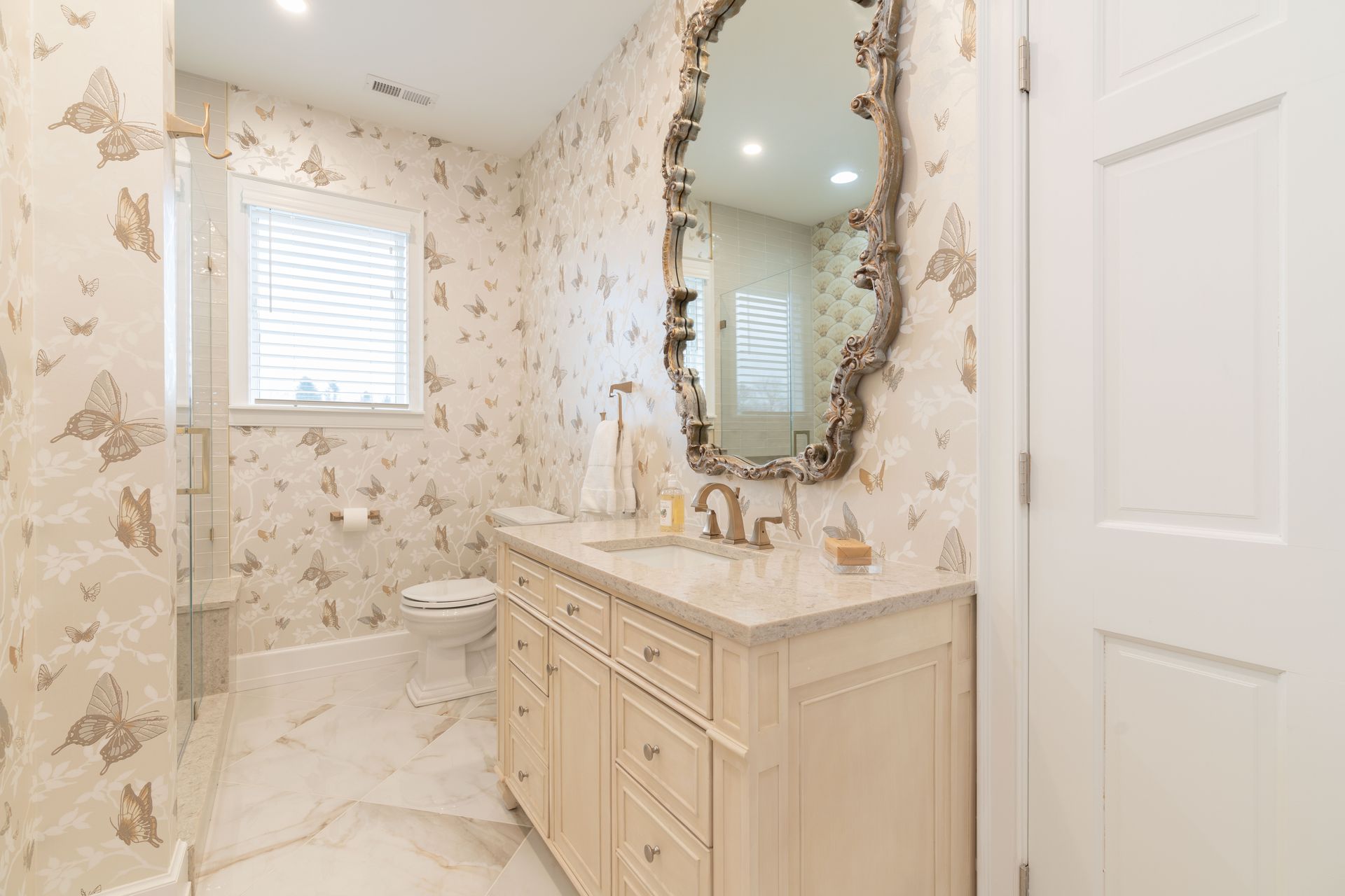 A bathroom with a sink , toilet , mirror and butterfly wallpaper.