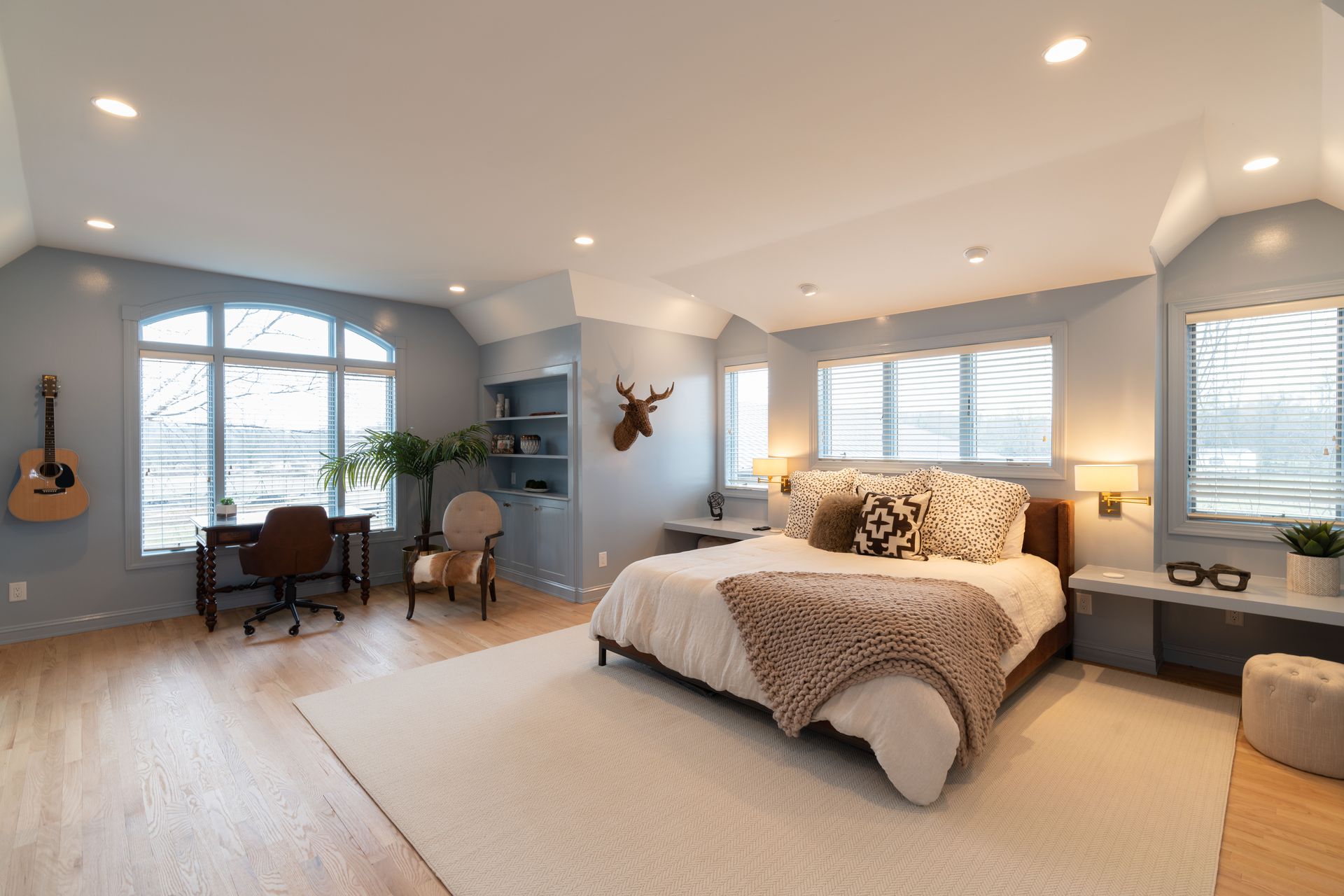 A bedroom with a large bed , desk , chair and guitar.