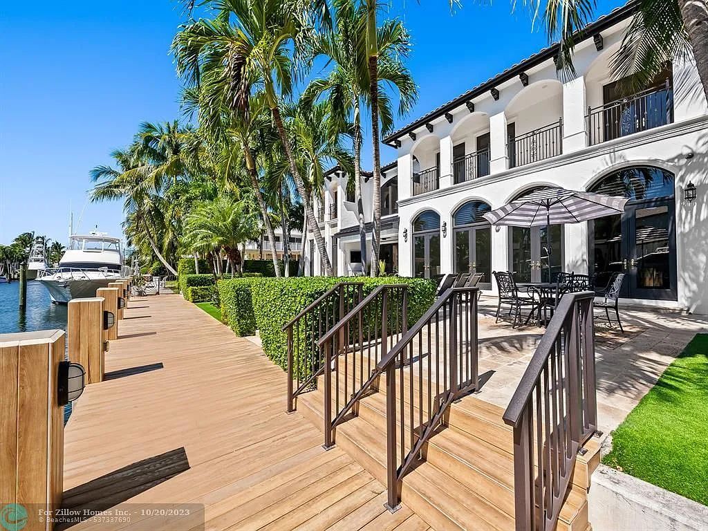 A large white house with a wooden deck and stairs leading up to it.