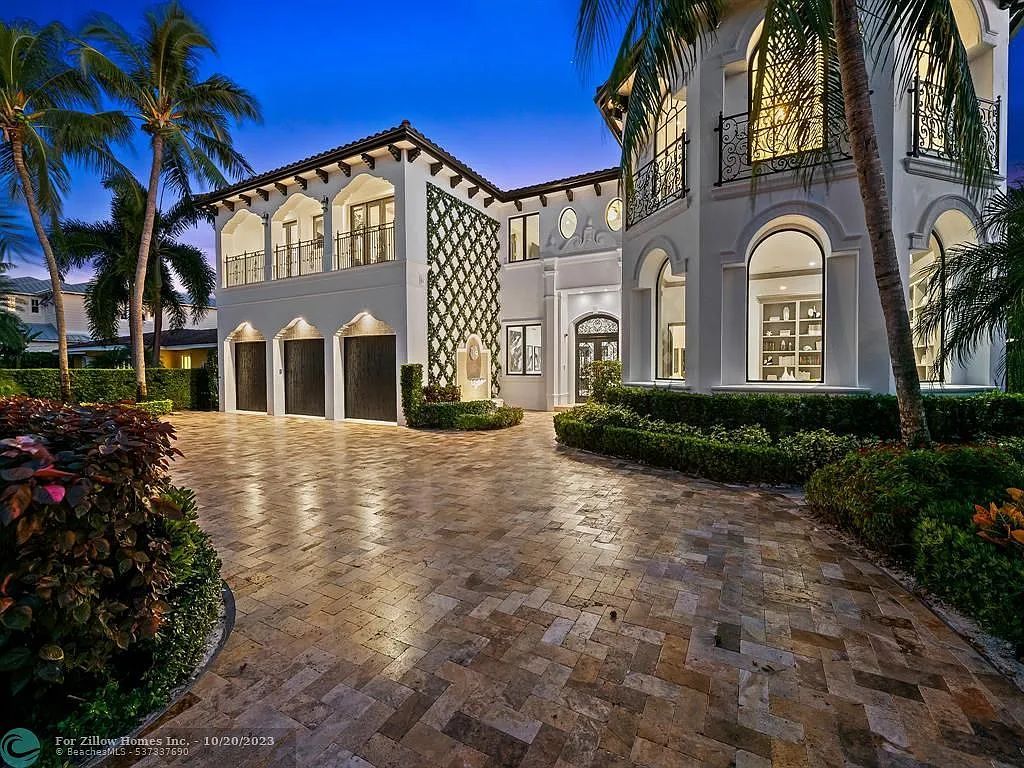 A large white house with a brick driveway and palm trees in front of it