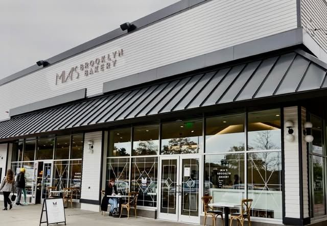 A white building with a black awning and tables and chairs in front of it.