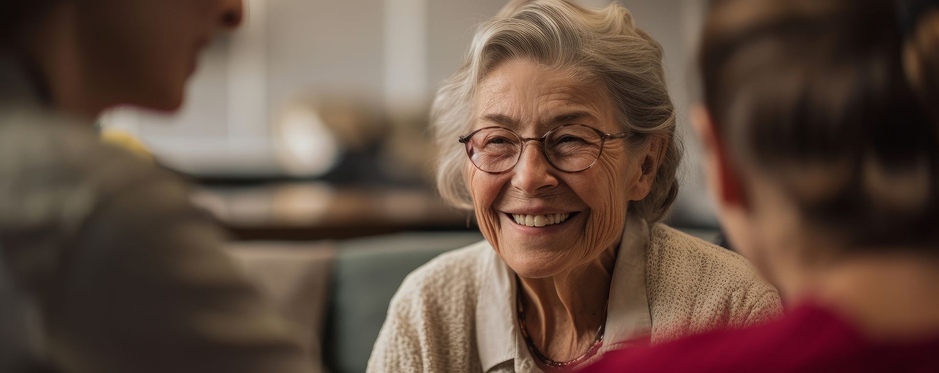 An elderly woman is smiling while sitting at a table with two other people.