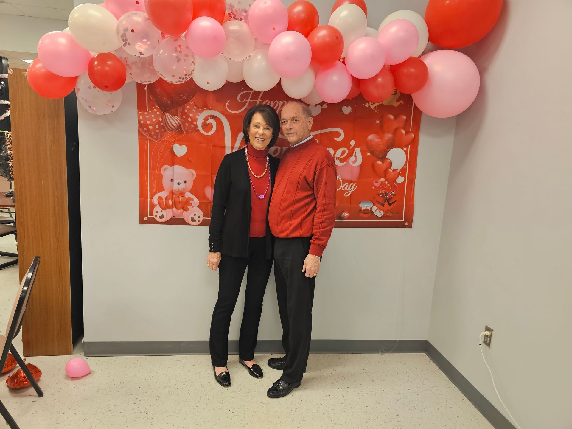 A man and a woman are posing for a picture in front of a wall with balloons.