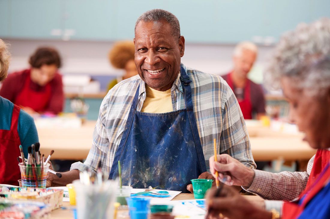 A man in an apron is sitting at a table painting a picture.