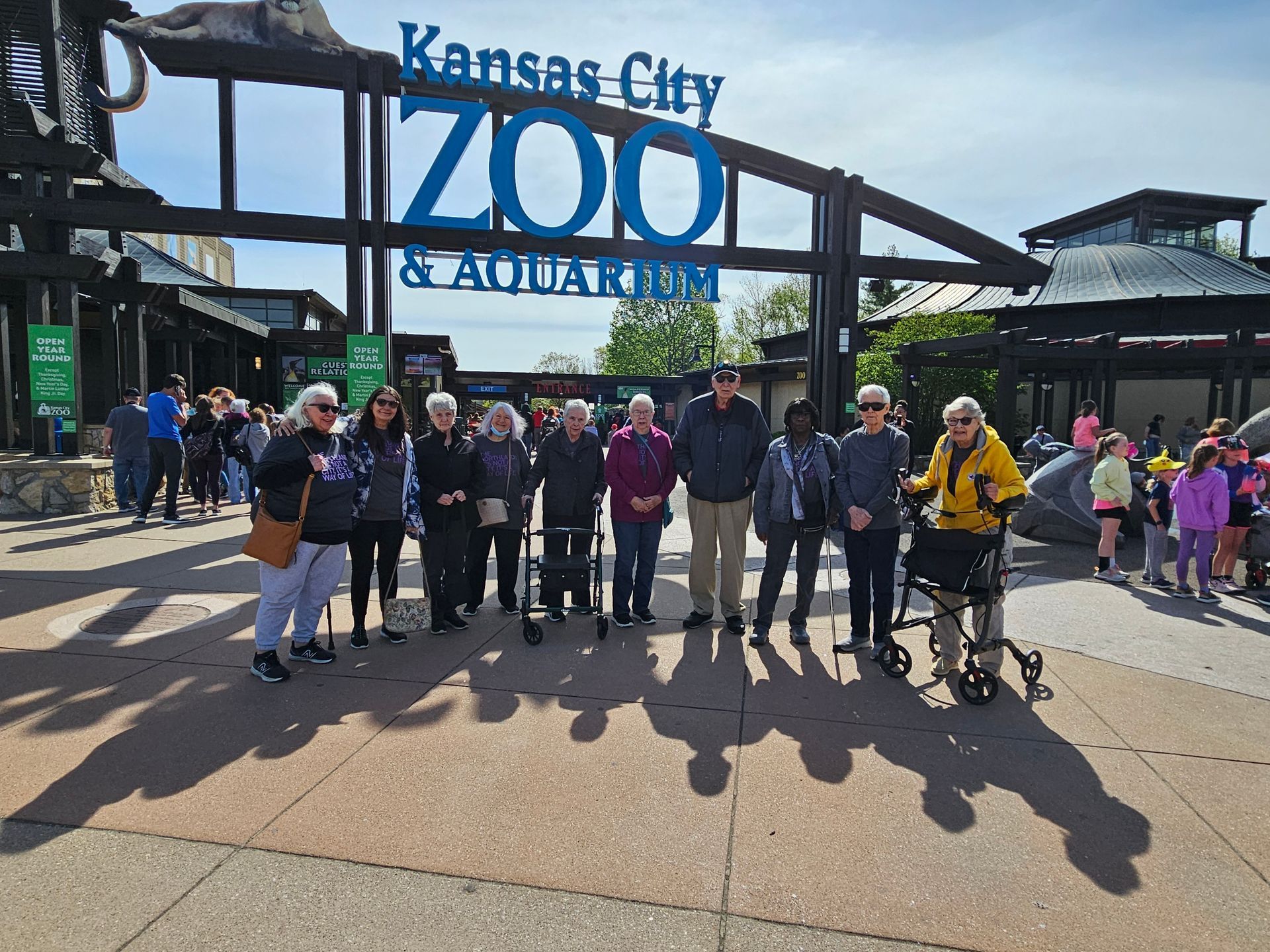 A group of people are standing in front of a zoo sign.