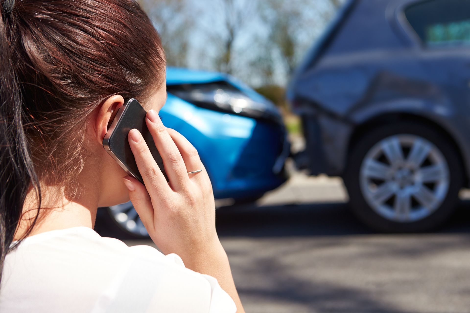 A woman is talking on a cell phone in front of a car accident.