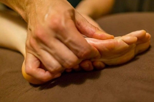 Hands massaging a bare foot on a brown surface