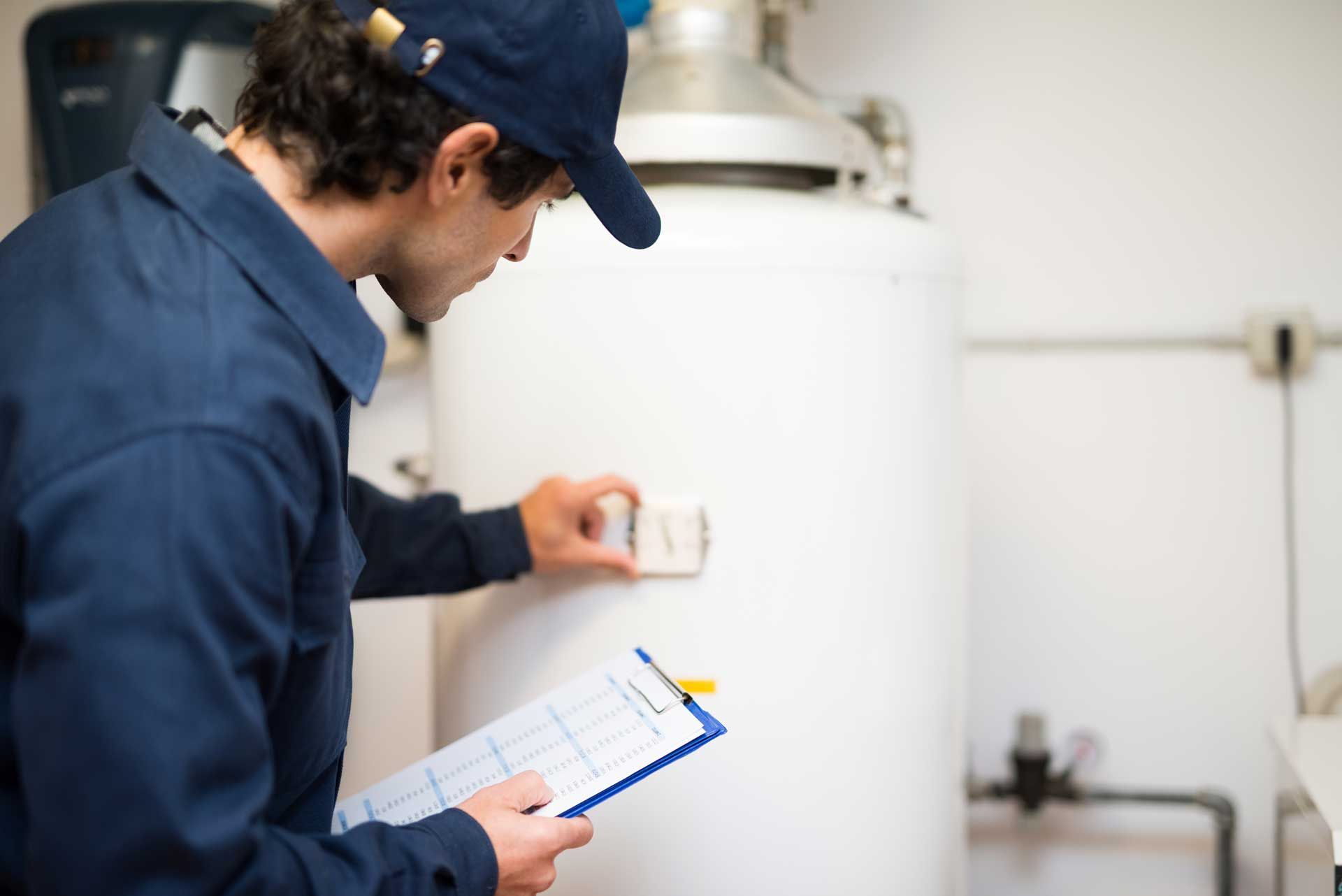 Plumber in blue uniform inspects a water heater, holding a clipboard in a utility room.