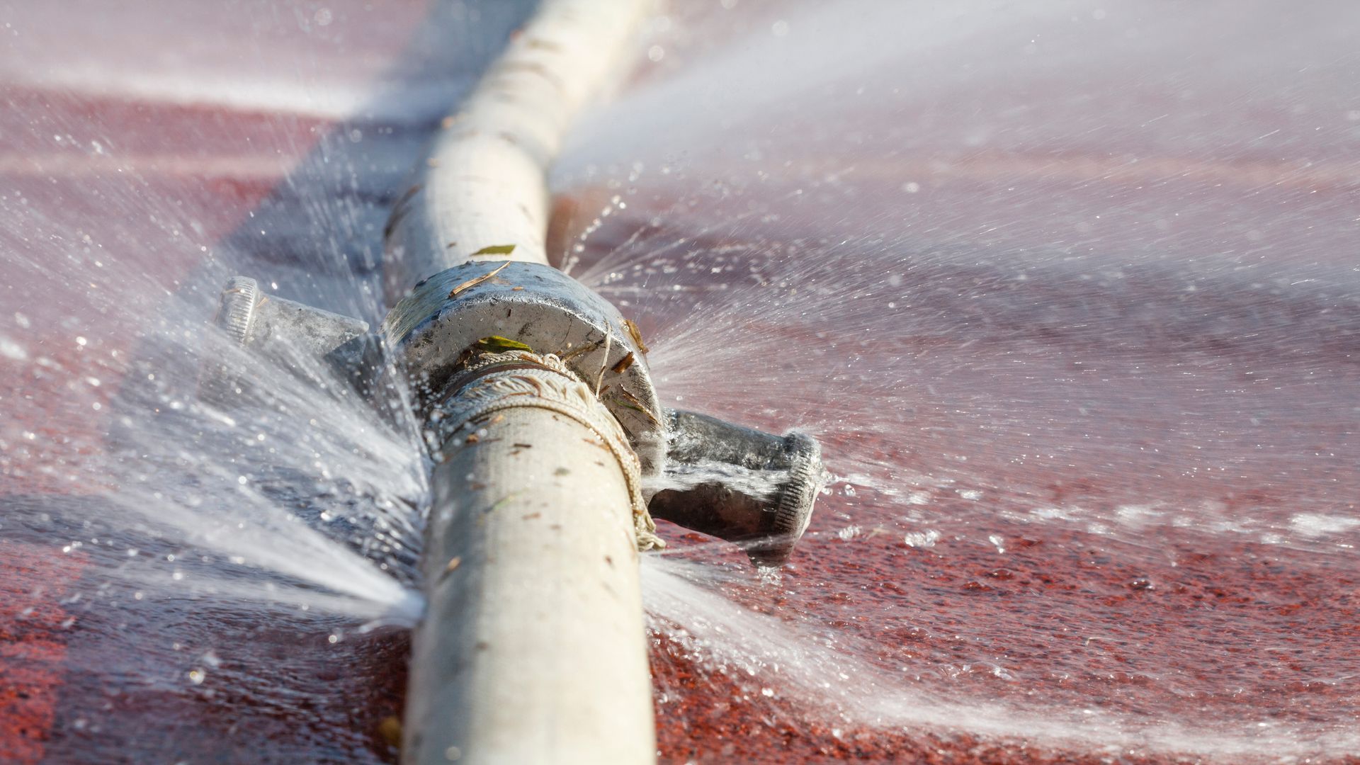 Leaking hose sprays water; a broken coupling sits on a red surface.