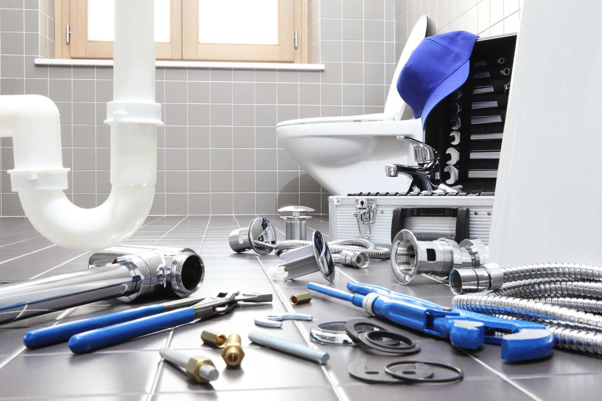 Plumbing tools and fittings scattered on a bathroom floor beside a sink and toilet under repair Plumbing tools and fittings scattered on a bathroom floor beside a sink and toilet under repair