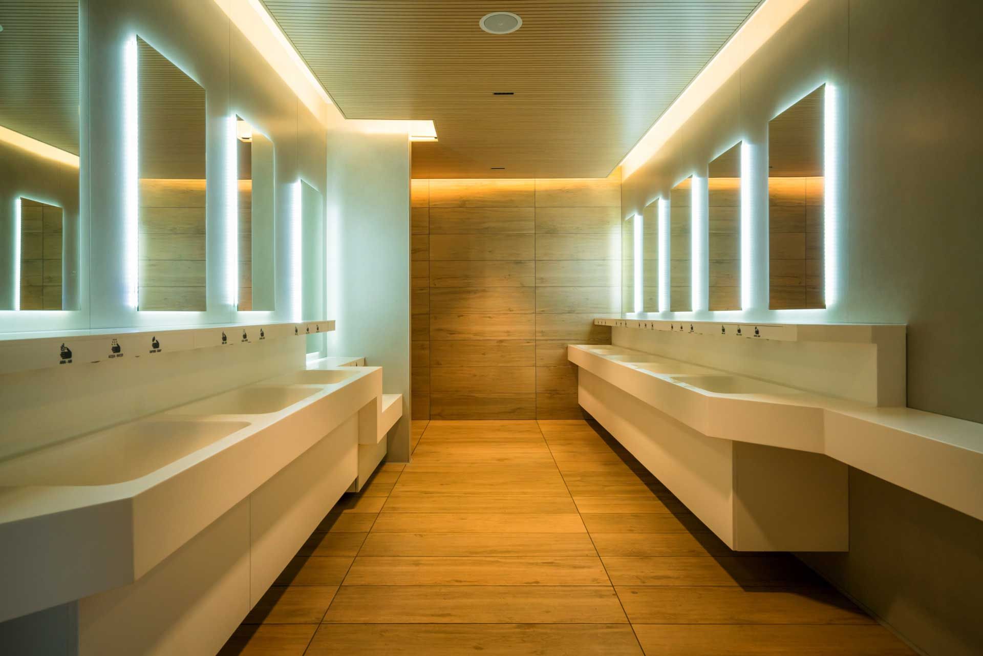 Modern public restroom with white sinks, mirrors, and warm lighting.
