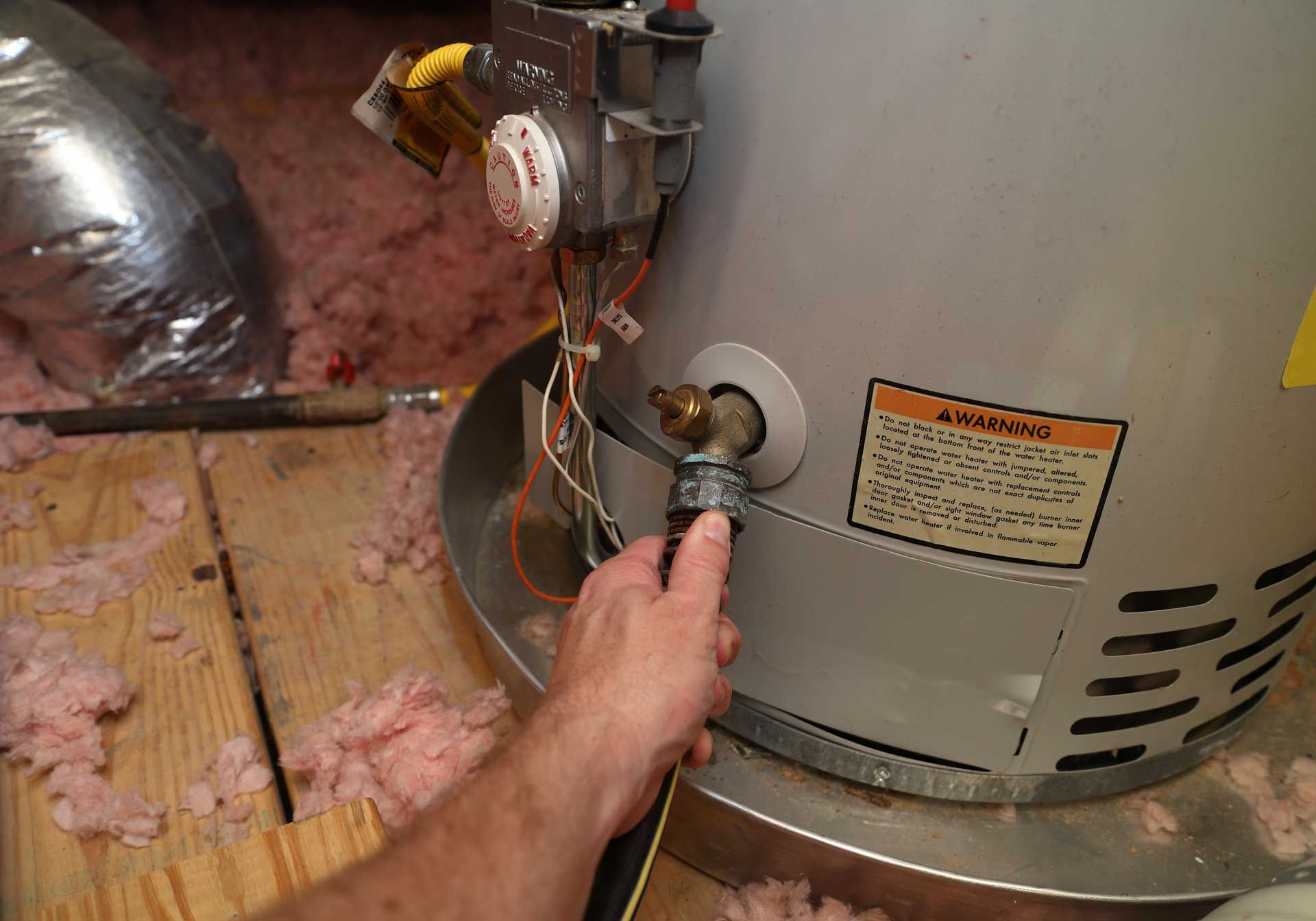 Hand tightening a hose connection on a water heater in an unfinished attic.