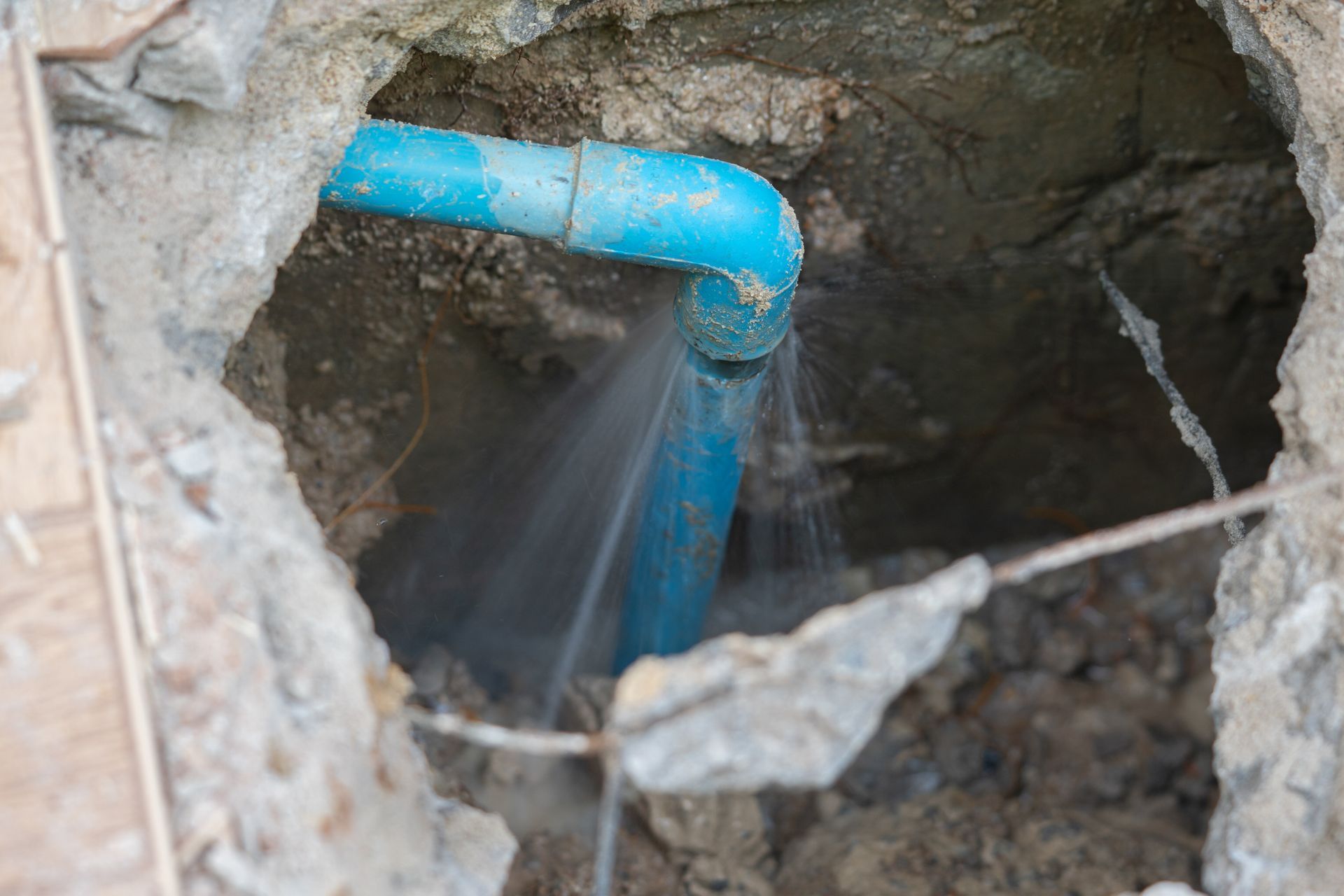 Leaking blue pipe in a hole, water spraying.