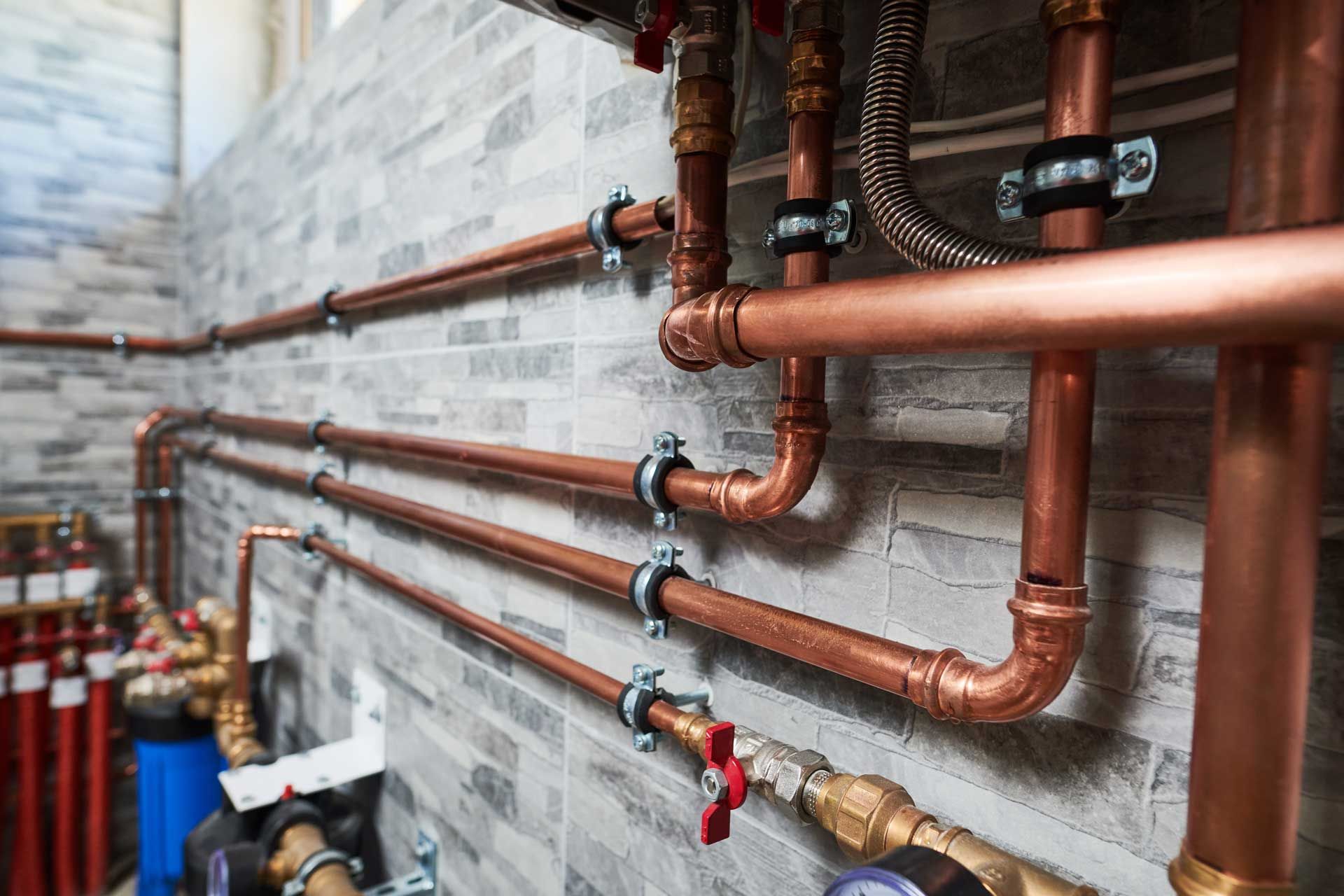 Copper pipes installed along a gray tiled wall, with various valves and fittings.