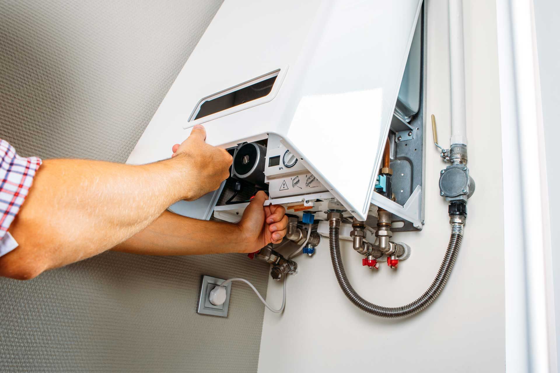 Person working on a white wall-mounted boiler, opening the panel to access the internal components.