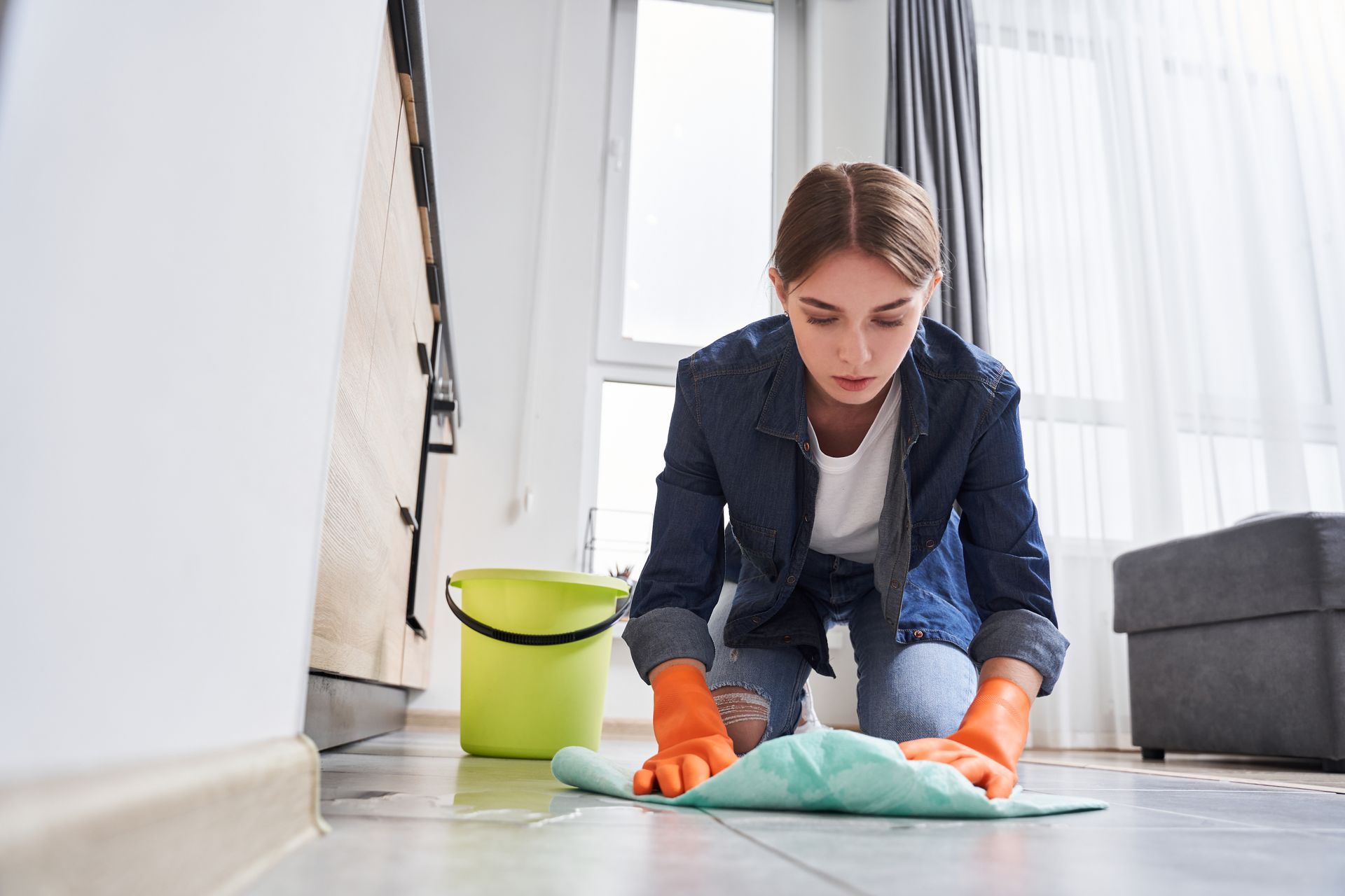 Person mopping a concrete floor with a red mop and bucket in a basement.