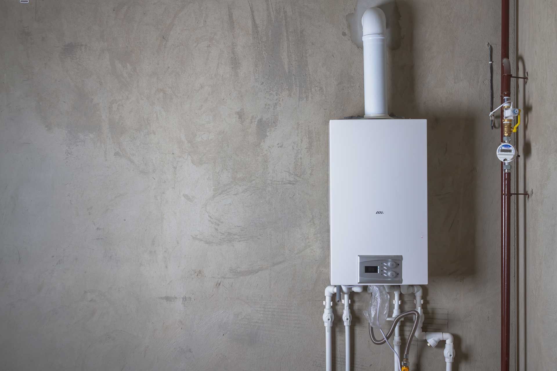 White wall-mounted boiler with pipes against a gray concrete wall.