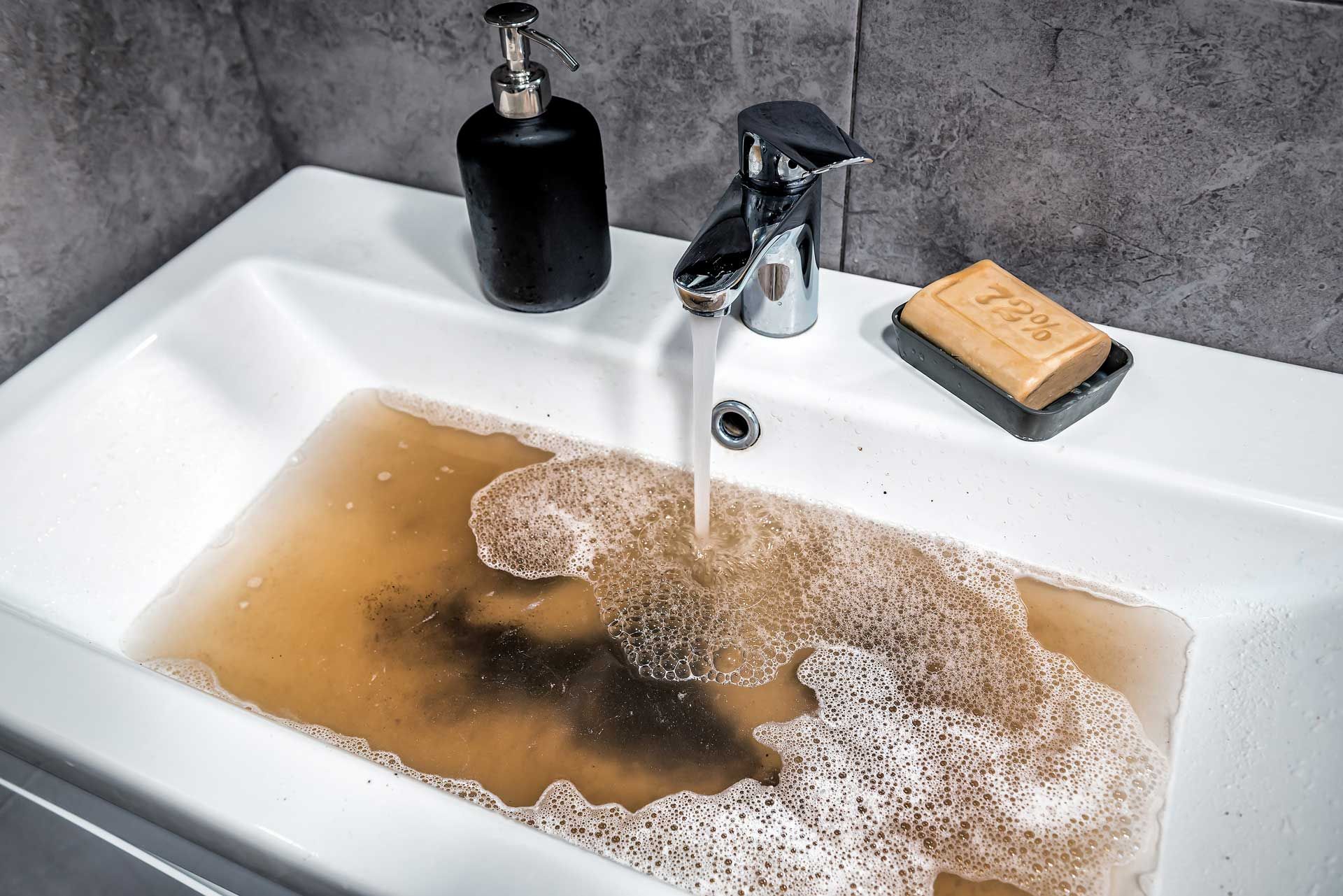 White sink filled with murky brown water; faucet running; soap and dispenser present.