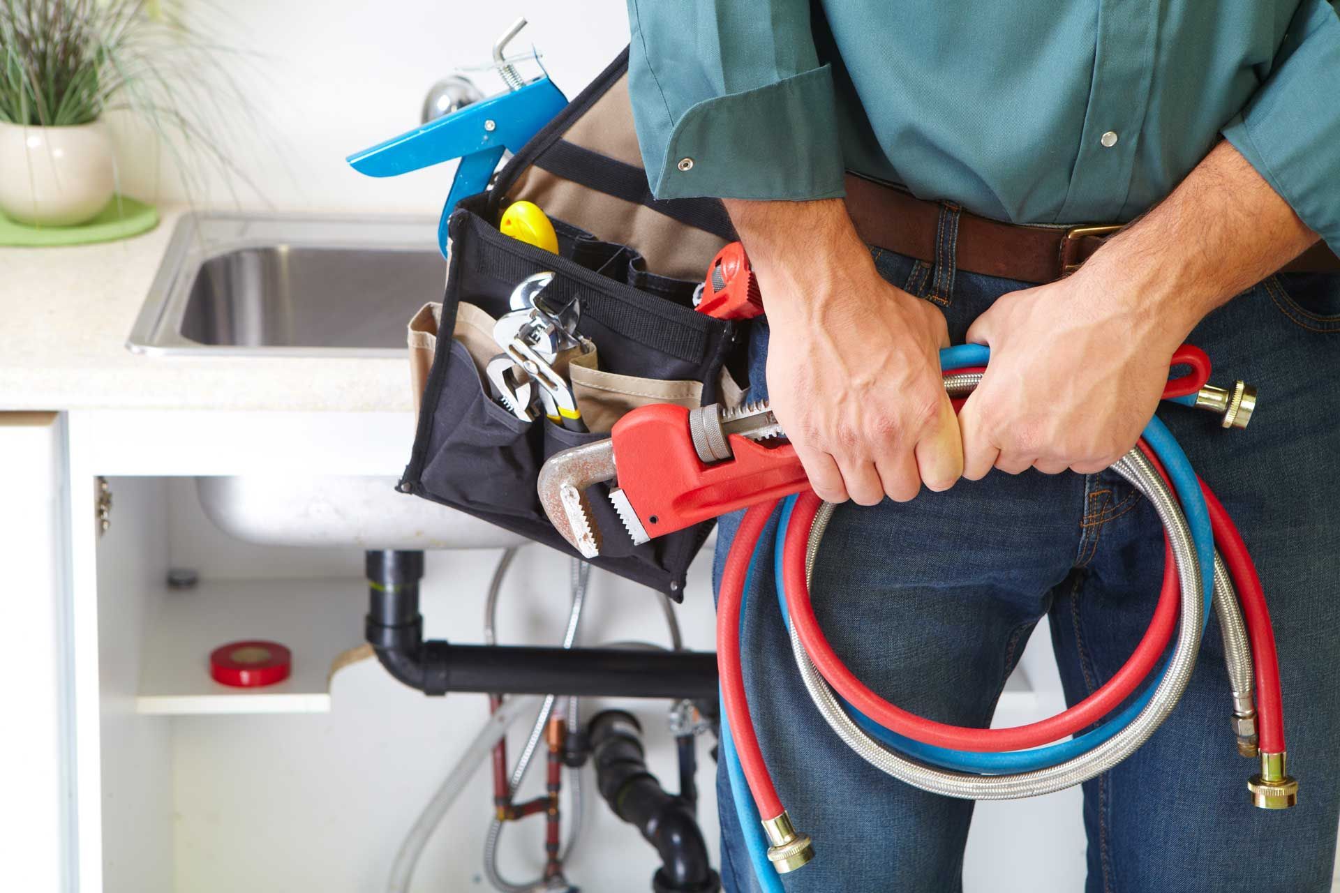 Plumber holding tools and hoses near a kitchen sink.