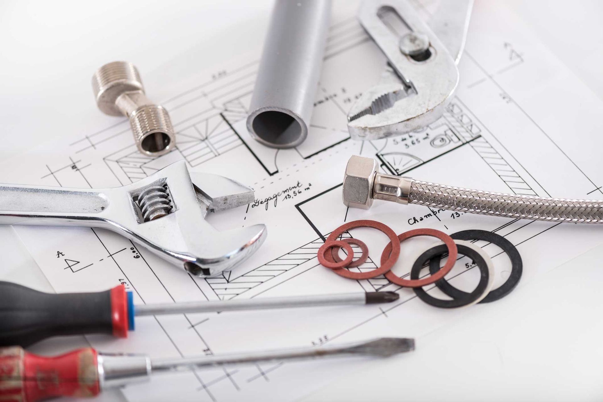 Plumbing tools and fittings on blueprints, including a wrench, pipes, and screwdrivers Plumbing tools and fittings on blueprints, including a wrench, pipes, and screwdrivers