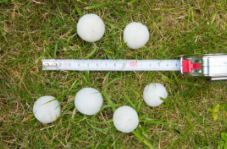 Different sizes of hail on grass with a tape measure in Cheyenne, WY after a hail storm.